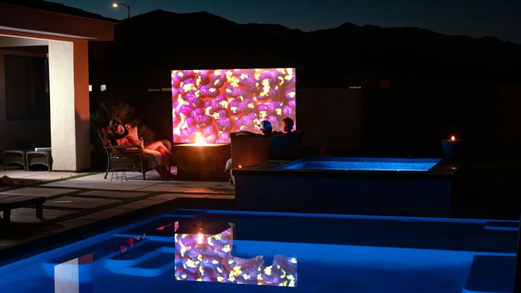 vier Leute sitzen draußen am Pool und schauen auf eine Projektionswand