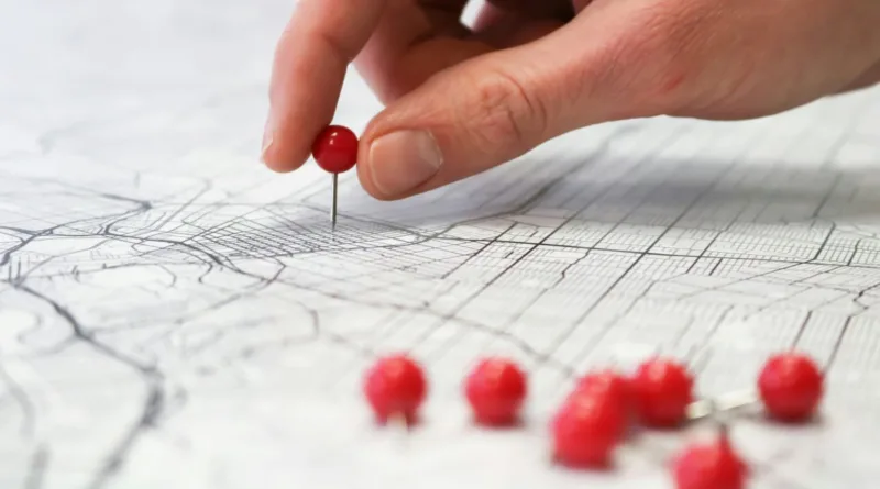 eine Hand steckt einen Pin in eine Karte