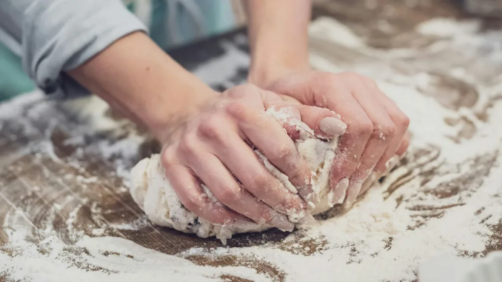 zwei Frauenhände kneten Teig in Mehl