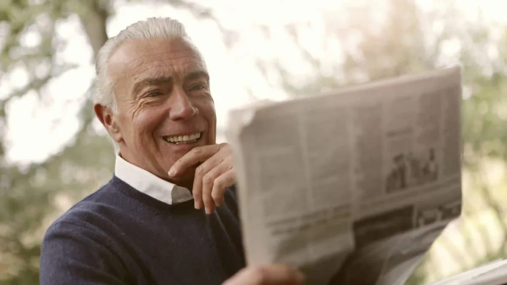 älterer Mann liest Zeitung und lächelt