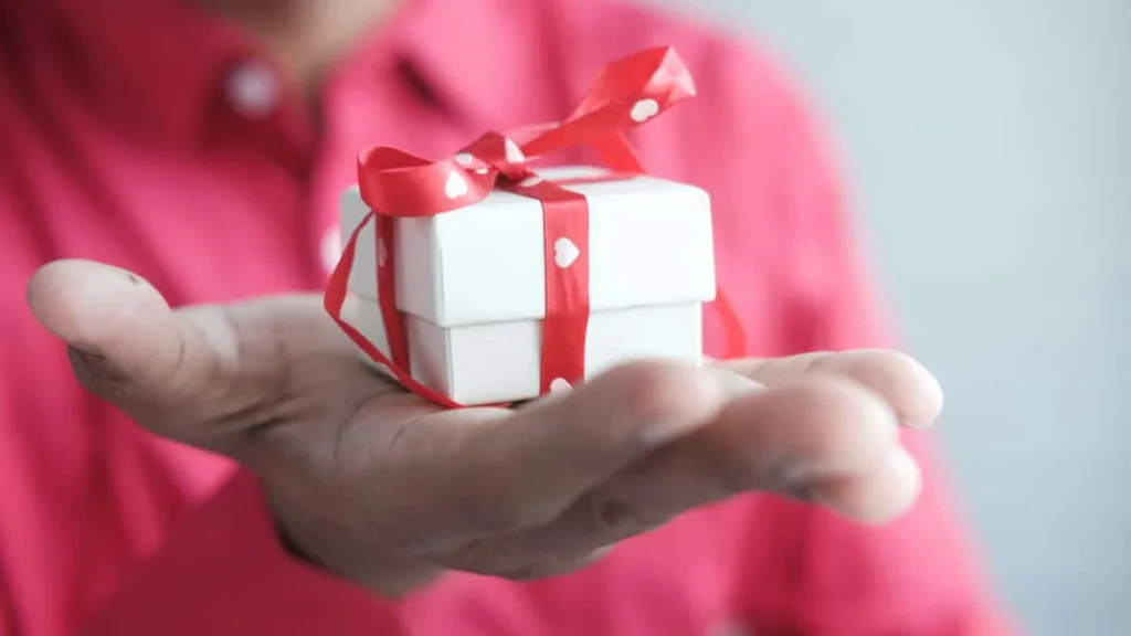 Männerhand mit einem kleinen weißen Geschenk mit roter Schleife