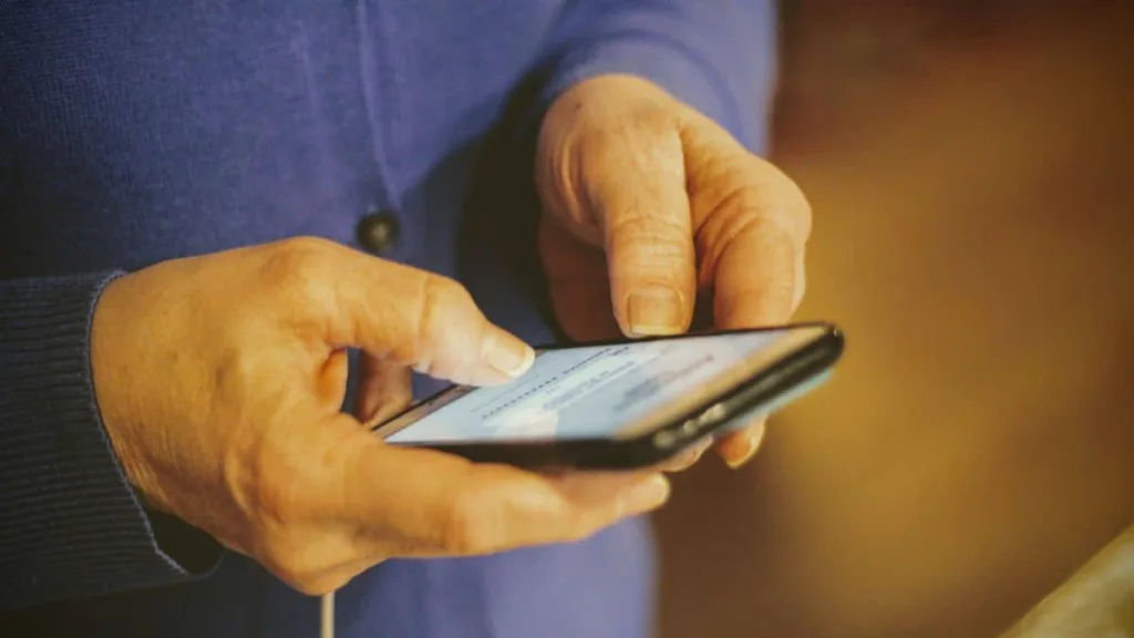man sieht, wie ältere Hände ein Handy bedienen