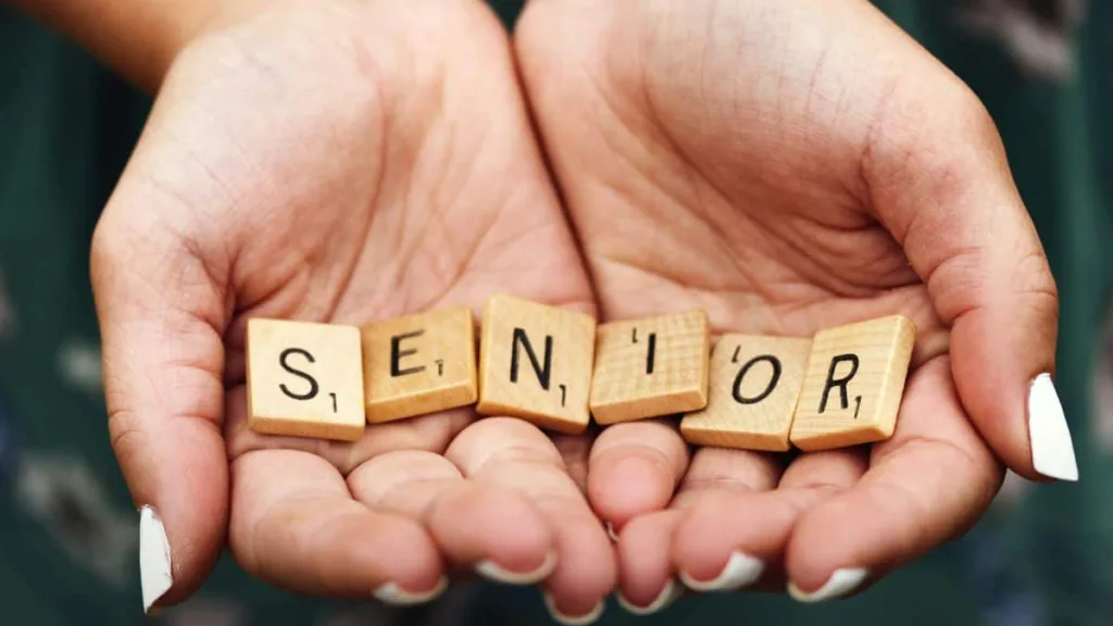 Zwei ältere Hände formen eine Schal und halten Dominosteine mit dem Wort Senior