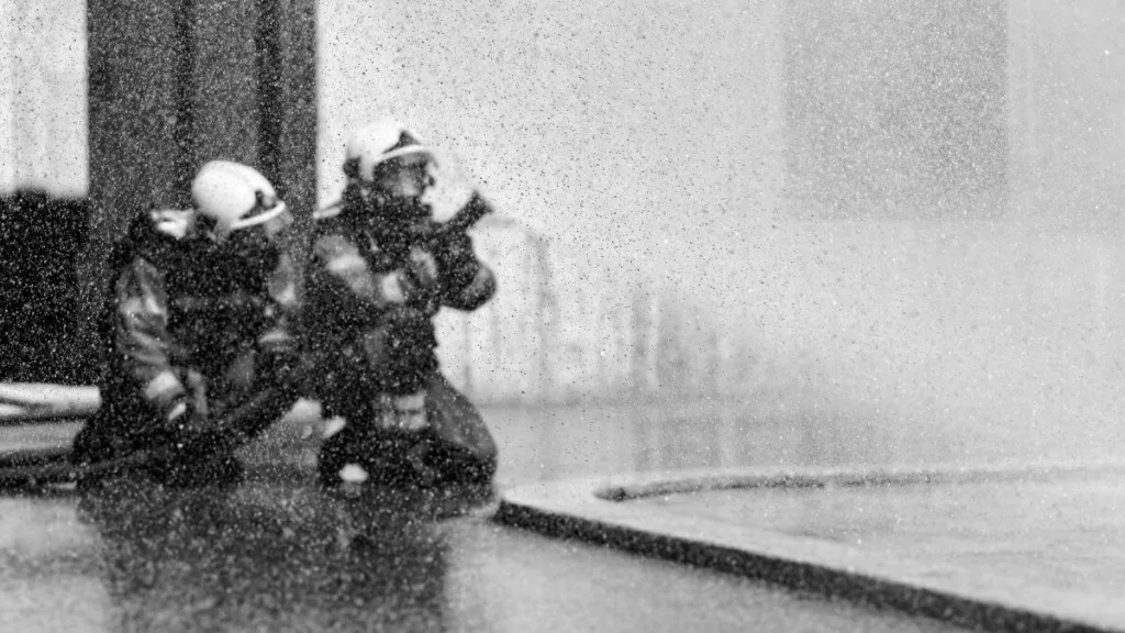 Farbloses Foto von zwei Feuerwehrmännern, die einen Schlauch halten