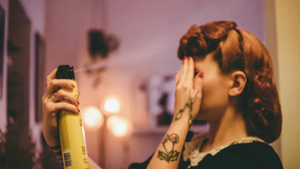 Eine Frau hält sich die hand vor die Augen und benutzt Haarspray für ihr Pony