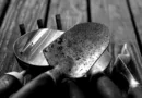 Pflanzschaufel, Handgrubber und Gartenkelle aus Metall mit Griffen auf verwitterter Holzoberfläche, schwarz/weiß dargestellt