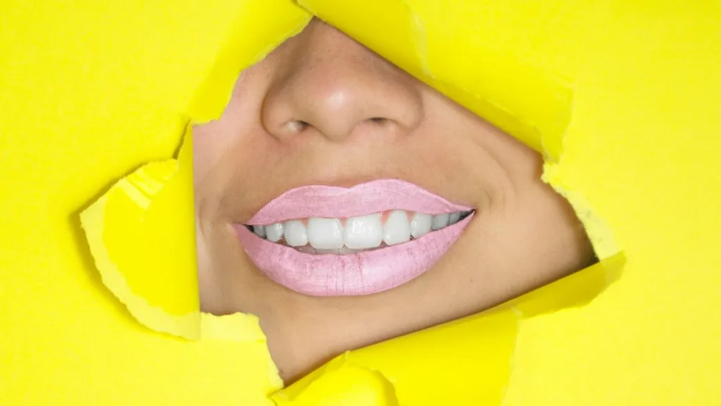 ein lächelnder Frauenmund mit viel Lippenstift schaut durch ein Loch aus Papier