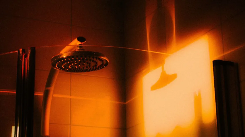 ein Duschkopf wird durch die Sonne angestrahlt und wirft einen Schatten auf die Wand