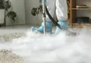 Person steht in Schutzkleidung auf einem Teppich, während dichter Dampf aus einem Bissell Reinigungsgerät aufsteigt