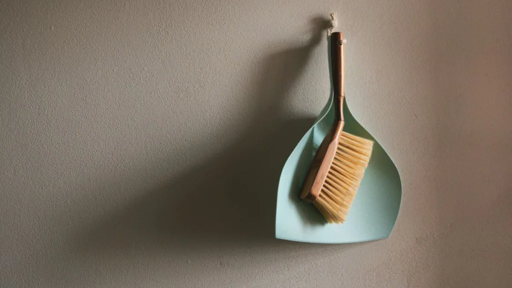 ein Kehrblech und ein Handfeger hängen an einer Wand