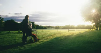 Eine ältere Frau wird im Rollstuhl Richtung Sonne geschoben