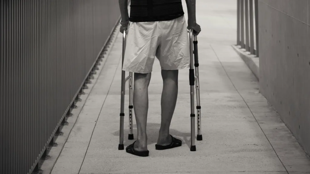 die Beine eines älteren Mannes mit einer Gehhilfe von hinten dargestellt, 