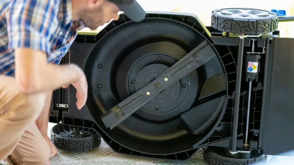 ein Mann  schaut sich das Rotiermesser eines Rasenmähers an