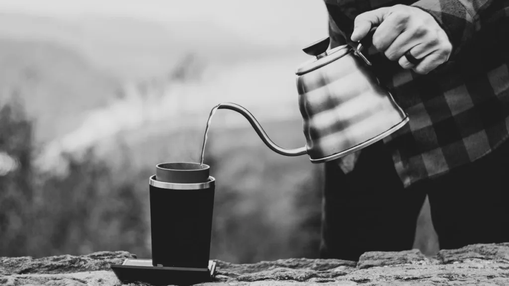 ein Mann gießt Outdoor Wasser in seinen Thermobecher aus einem Wasserkessel