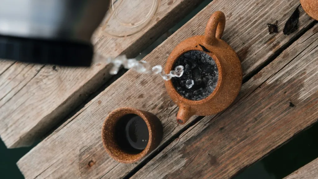 in eine Kanne aus Keramik wird heißes Wasser aus einem Wasserkocher gegossen