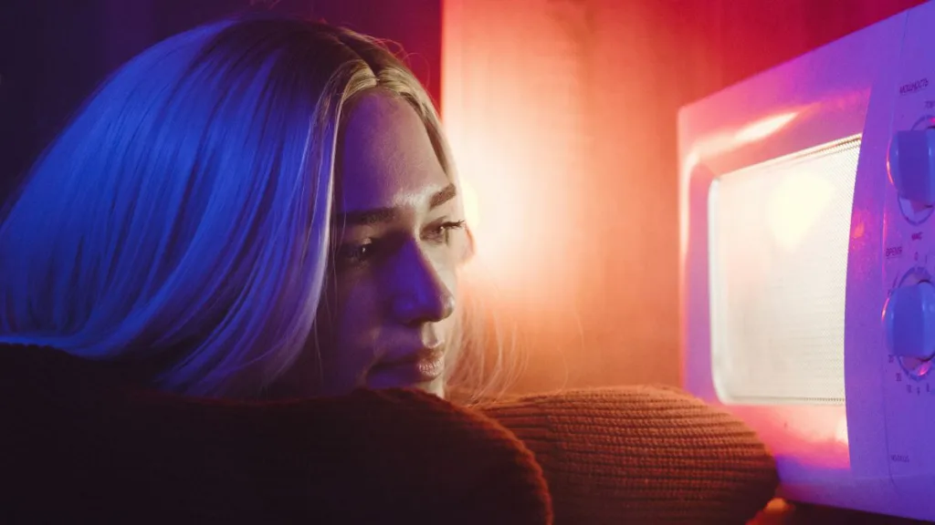 eine blonde Frau schaut in eine leuchtende Mikrowelle