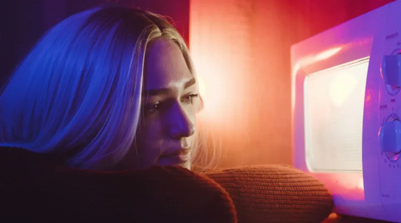 eine blonde Frau schaut in eine leuchtende Mikrowelle