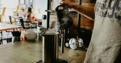 ein Mann gießt heisses Wasser aus einen Wasserkocher in ein Edelstahlgefäß