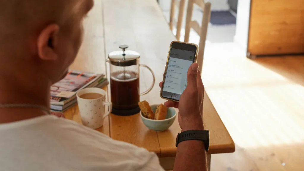 ein Mann schaut während des Frühstücks auf sein Handy und schaut sich seine Gesundheitsdaten an