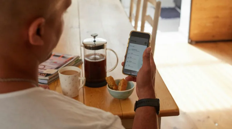 ein Mann schaut während des Frühstücks auf sein Handy und schaut sich seine Gesundheitsdaten an