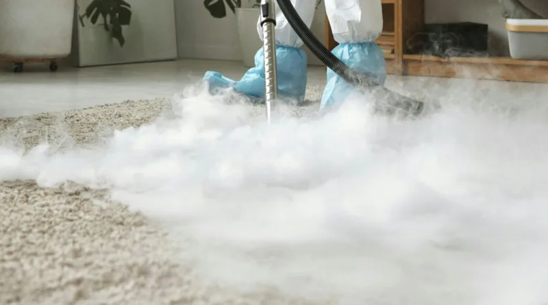 ein Mann in Schutzanzug säubert mit viel Dampf einen Teppich