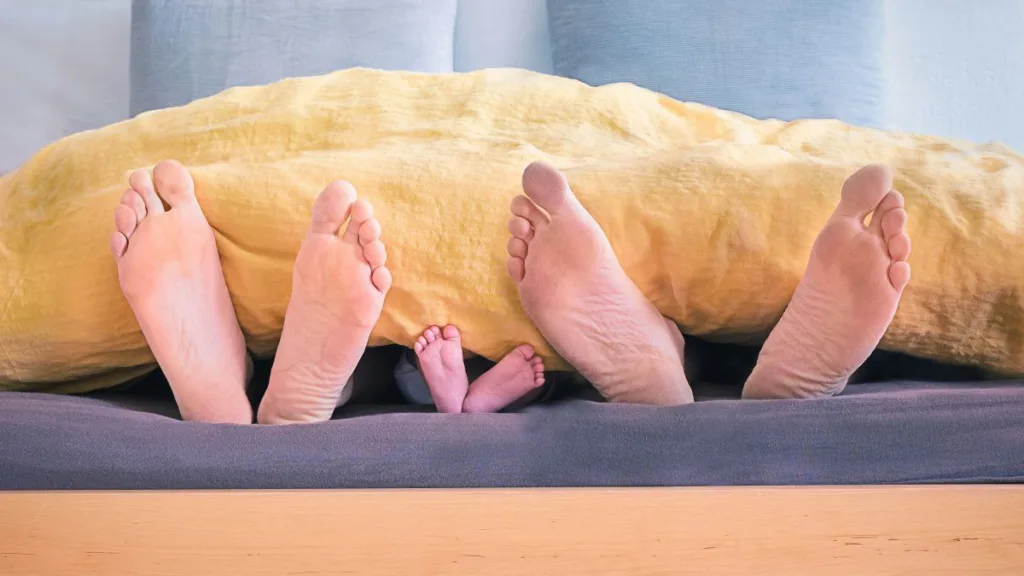 die Füße einer Frau, eines Kleinkindes und eines Mannes schauen unter einer Bettdecke hervor