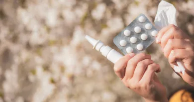 die Hände einer Frau mit Tabletten, Nasenpsray und einem Taschentuch