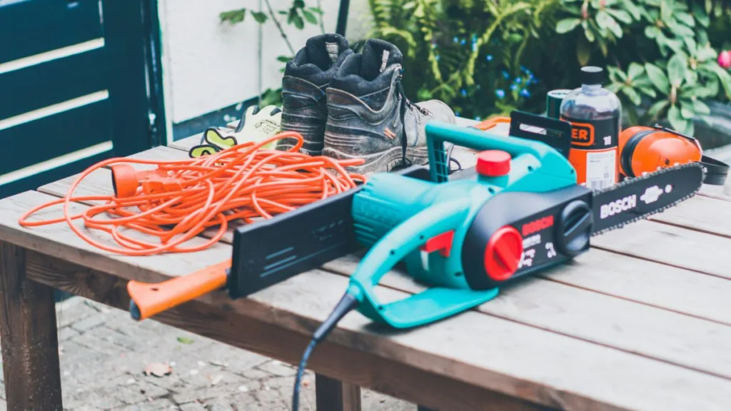 eine Elektro-Kettensäge und diverses Arbeitszubehör liegen auf einem Tisch