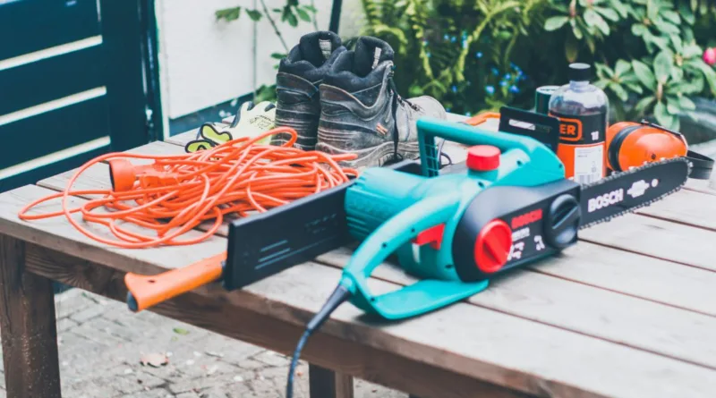 eine Elektro-Kettensäge und diverses Arbeitszubehör liegen auf einem Tisch