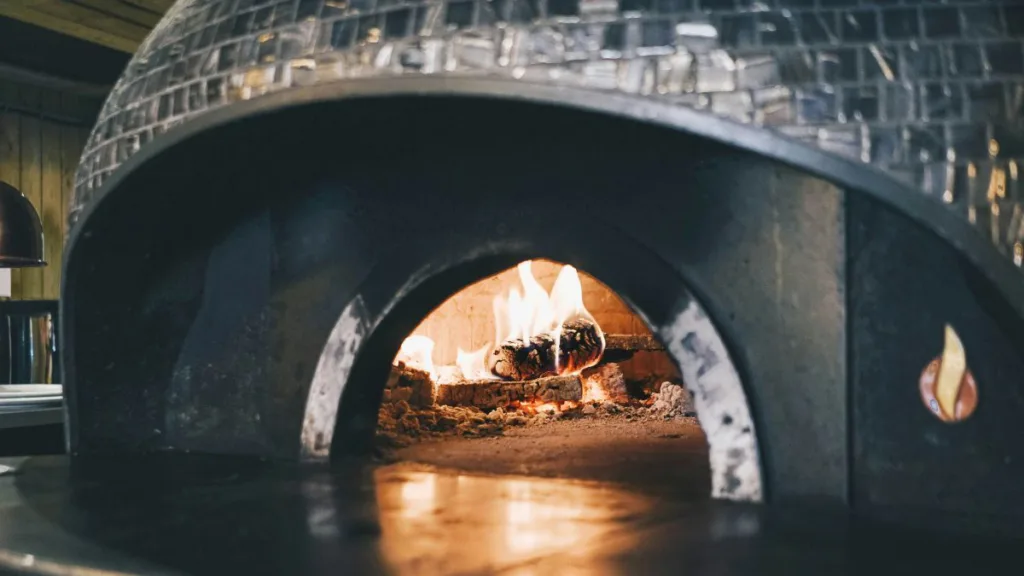 Traditioneller Pizzaofen mit Mosaik-Kuppel und brennendem Holzfeuer im Inneren