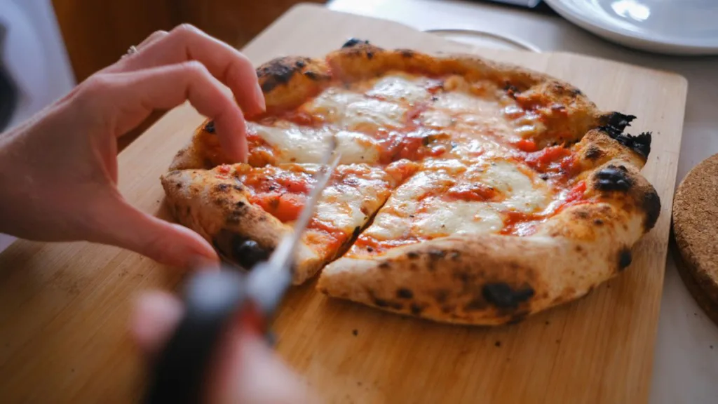 eine frisch zubereitete Pizza wird auf einem Holzbrettchen geschnitten