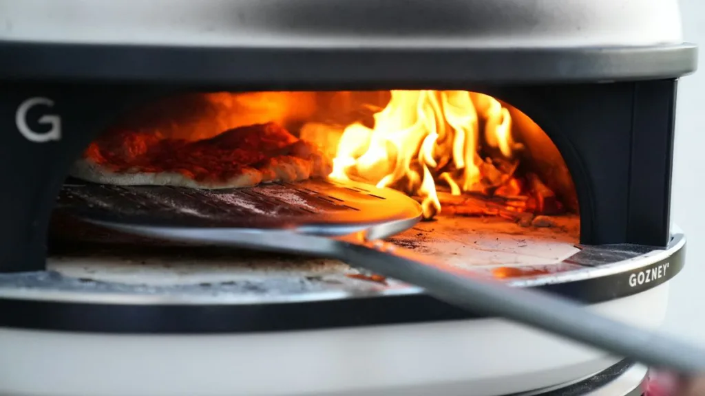 Pizza wird in einem Pizzaofen mit offener Flamme und einem Pizzaschieber gebacken
