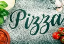 Mehl auf einem Tisch, wo das Wort Pizza geschrieben steht und Pizzazutaten daneben angeordnet