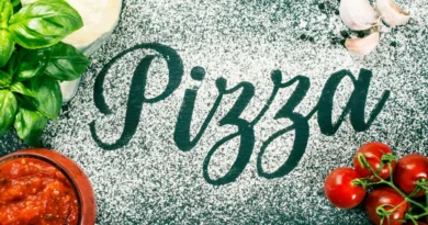 Mehl auf einem Tisch, wo das Wort Pizza geschrieben steht und Pizzazutaten daneben angeordnet