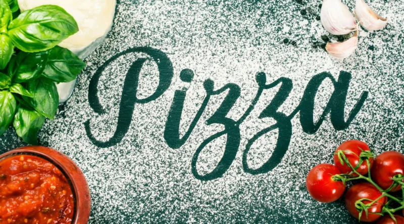 Mehl auf einem Tisch, wo das Wort Pizza geschrieben steht und Pizzazutaten daneben angeordnet