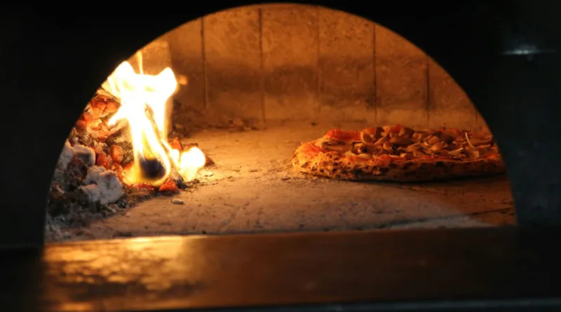 Ansicht in ein Holzkohleofen, liks das Feuer und rechts eine Pizza