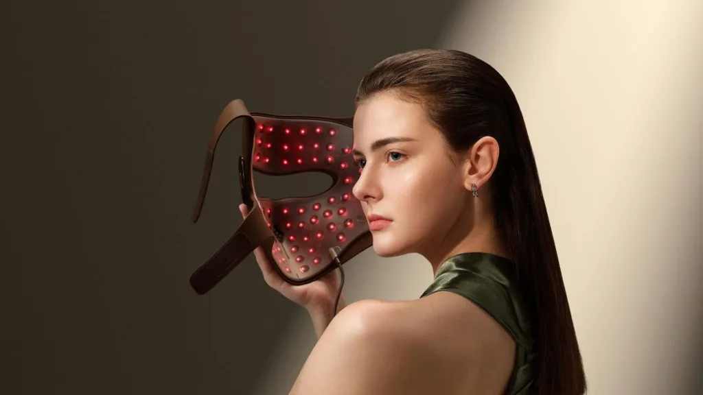 eine Frau hält eine der LED-Lichtmasken in der Hand und setzt sie gleich auf