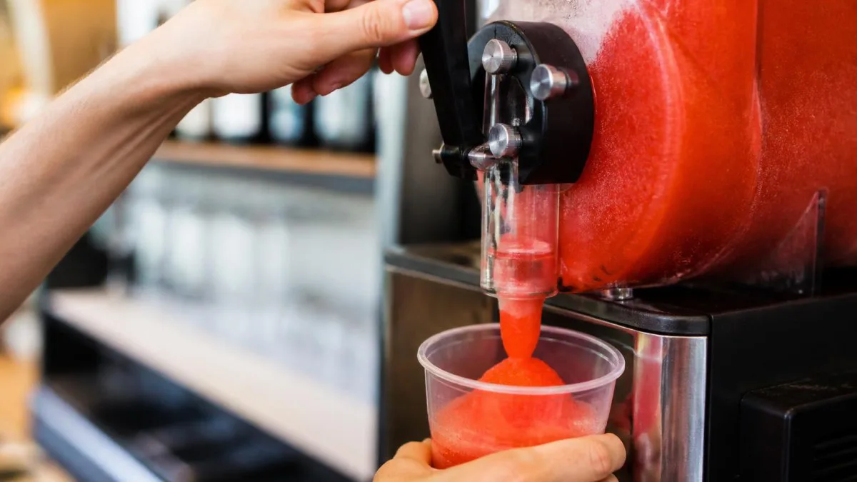 Hand bedient Zapfhahn einer Slushmaschine, Slush läuft in Glas