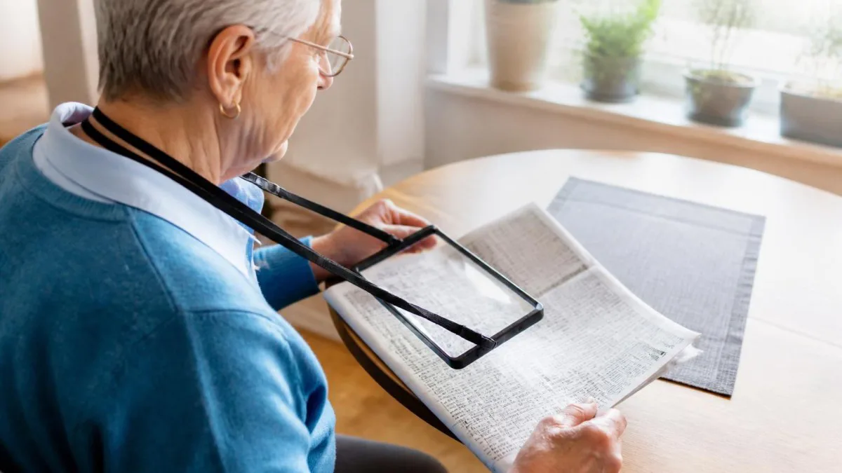 Senior sitzt am Tisch und liest Kleingedrucktes mit einer der Leselupen zum umhängen für Senioren
